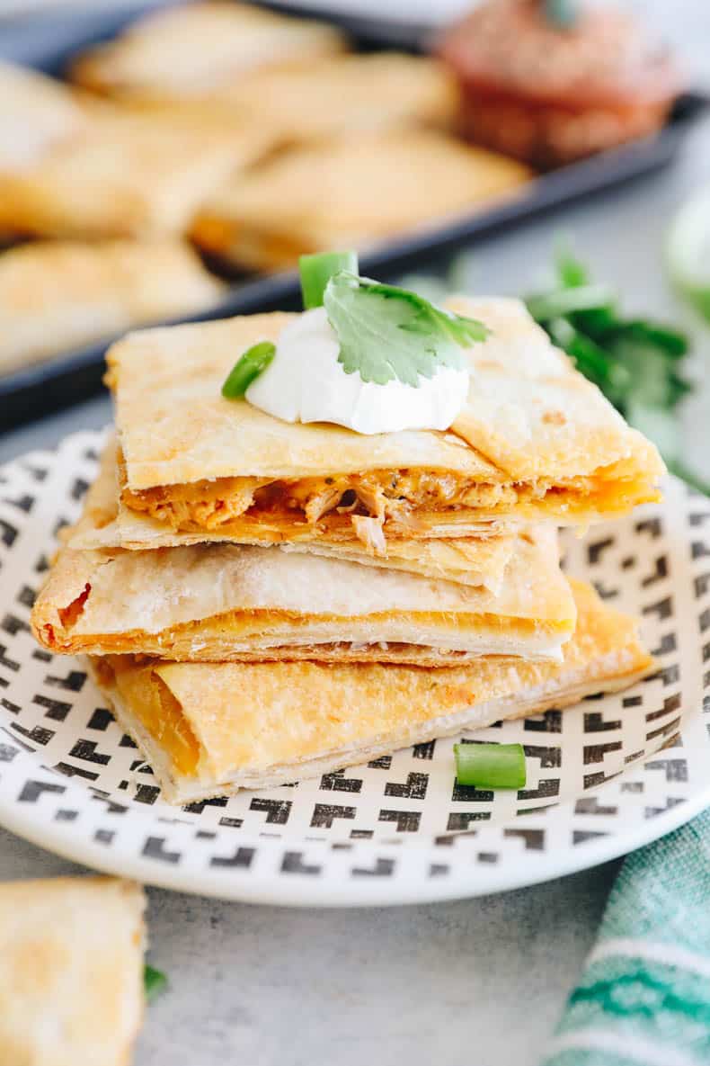 sheet pan quesadillas topped with sour cream, cilantro and green onion.