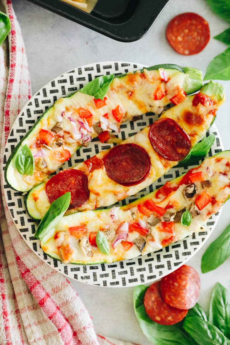 3 zucchini pizza boats with toppings on a black and white plate.