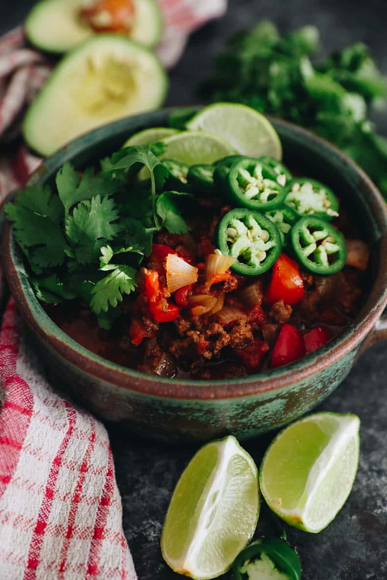No Bean Chili in a green bowl with sliced jalapeno, lime wedges and cilantro.
