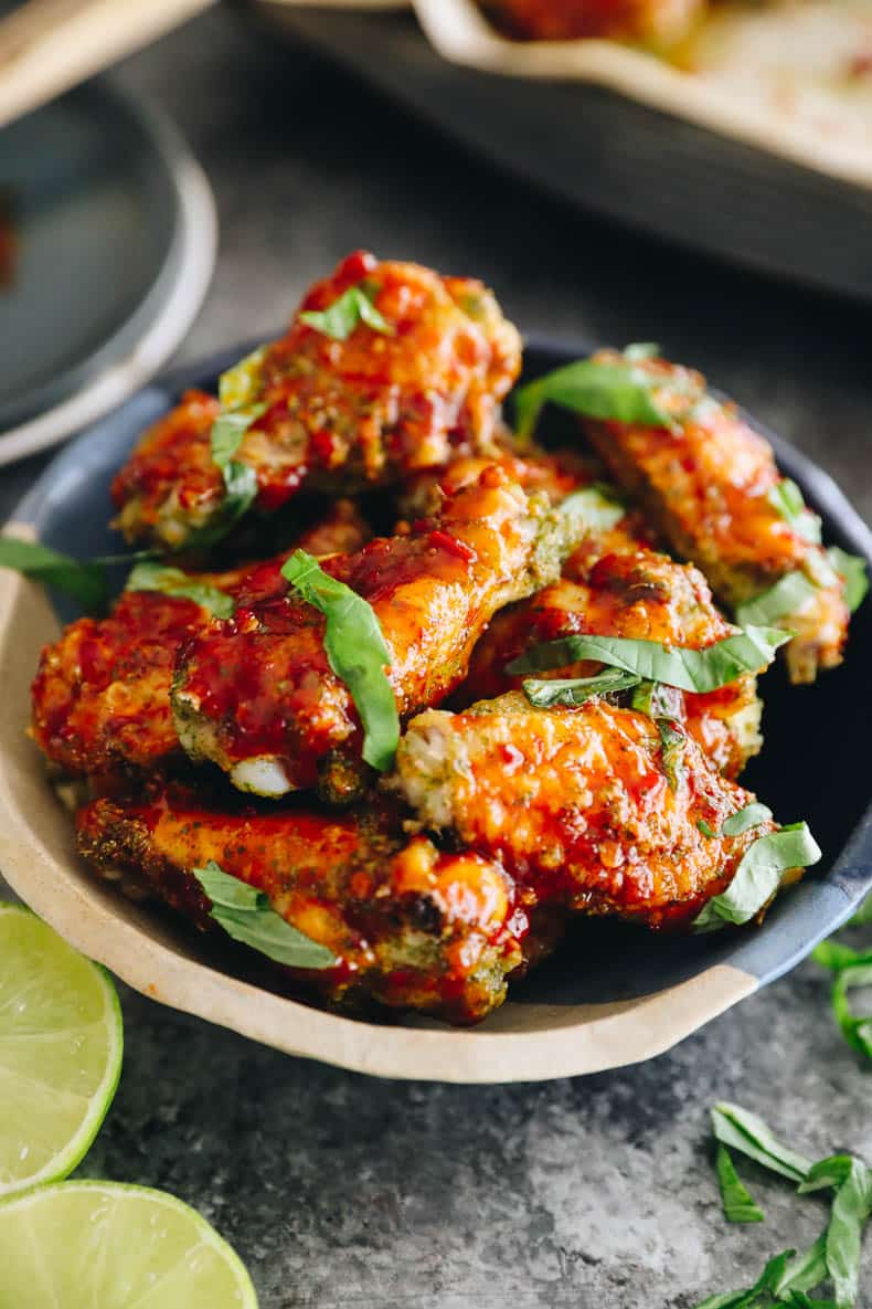 Baked thai chicken wings in a bowl topped with sprinkled thai basil.